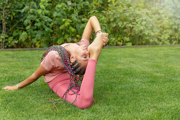 Flexible long haired girl performing gymnastic exercises in the garden. Horizontally. 