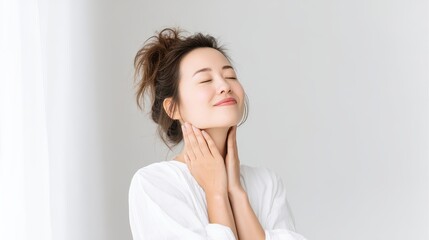 A serene woman enjoys a moment of self-care, gently touching her neck with a relaxed smile, showcasing the essence of wellness and tranquility in a minimalist, bright environment.
