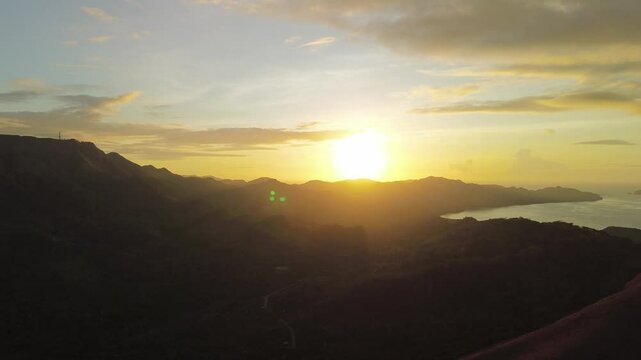 Aerial view circling softly over the hills near Mount Tapyas as the morning sun rises, casting warm golden light over the landscape in Coron, Palawan.