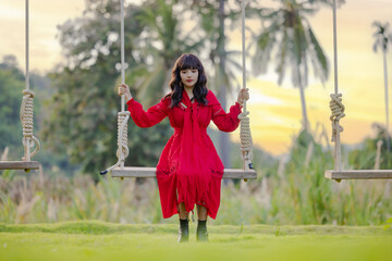 Beautiful young asian woman on a swinging on a swing at nature garden. Outdoor portrait of a smiling happy girl. Young woman enjoying freedom.