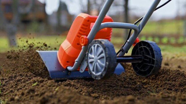 Woman preparing garden beds for planting using cultivator. Rotovator, garden tiller, rotary tiller close up. Cultivators break up compacted soil, improve its structure and aeration.