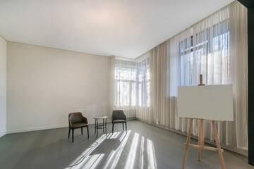 An empty living room with parquet floors and light walls. Windows with curtains. Unfurnished. The interior design is presented on an easel.