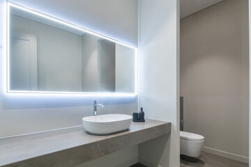 Elegant design of the bathroom, decorated in white and gray tones. Illuminated mirror over the sink bowl.