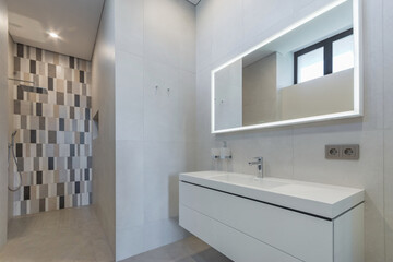 Modern design of the bathroom decorated with white tiles. A shower with a tropical watering can against the wall decorated with colorful tiles.