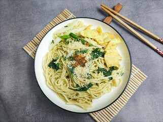 Mie Pangsit or Mie Ayam Pangsit. Popular noodles in Indonesia with minced chicken and green mustard toppings, complete with chopsticks and crackers. with a gray background