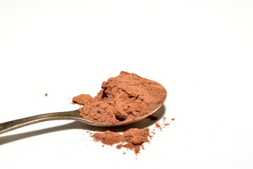 Cocoa powder in an iron spoon on a white background.