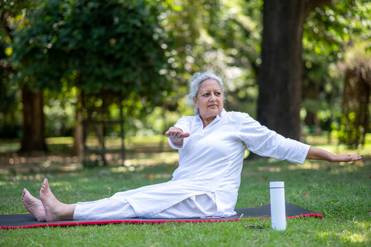Indian healthy senior woman doing yoga workout while sitting in different yoga poses at mat in the nature