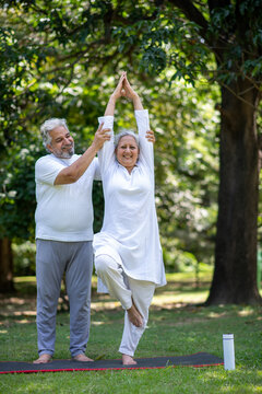 Indian senior couple doing Yoga while standing on yoga mat in the  nature greenery environment. Concept of senior health care after retirement insurance  