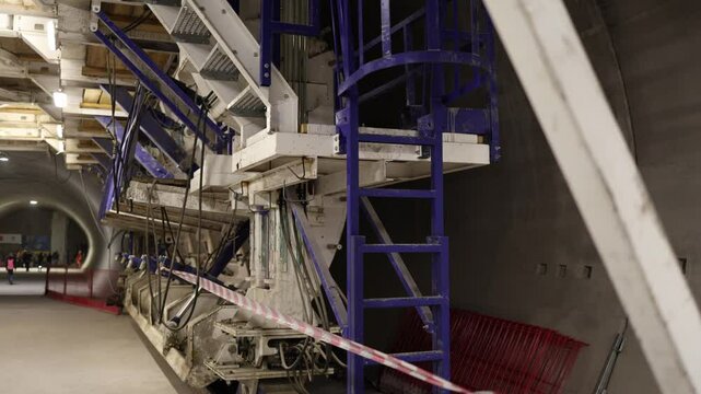 Underground military bunker construction large automated formwork system mounted to tunnel wall clean concrete surface under bright lights with safety barriers and electrical lines in place