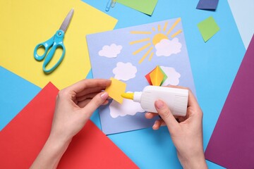 Woman making postcard on light blue background, top view. Child handmade craft