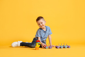 Naklejka premium Cute little boy playing with train toy on yellow background