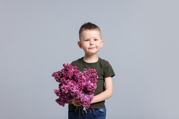 Little boy with bouquet of lilac flowers on light grey background