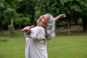 Indian happy senior woman spread her arms in environment nature like the wings of a bird. Happiness. Freedom. Elderly woman stands with one hand open in a park. Indian active old age at woman in park