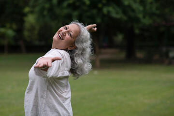 Indian happy senior woman spread her arms in environment nature like the wings of a bird. Happiness. Freedom. Elderly woman stands with one hand open in a park. Indian active old age at woman in park © Pix4Ads