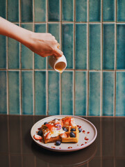 Waffles with fresh berries. A hand pouring maple syrup on waffles with topping whipping cream and berries (strawberries and blueberries)