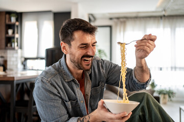 Cheerful man enjoying noodles at home: eating with a smile