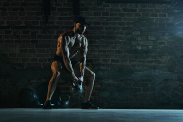 Man performing kettlebell movement in squatting stance during workout with muscle focus at morn...