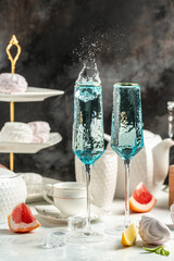 Elegant splashes of blue cocktail in champagne flutes with gourmet desserts and citrus fruits