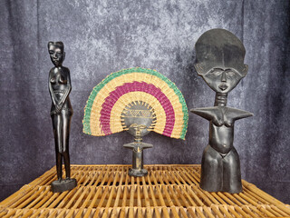 African artifacts resting on a wicker table. The composition is composed of three statuettes carved...