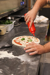 Pizzaiolo mentre condisce con dell'olio d'oliva una pizza margherita tradizionale napoletana con sugo di pomodoro, mozzarella di bufala e basilico fresco