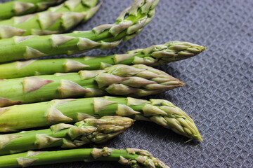 Green asparagus on black textile background. Asparagus close up. Bunch of fresh green asparagus on black fabric. Veggies background. Vegetables on kitchen towel