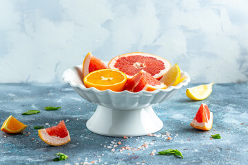 Fresh citrus fruits in a white pedestal bowl on a blue textured surface.