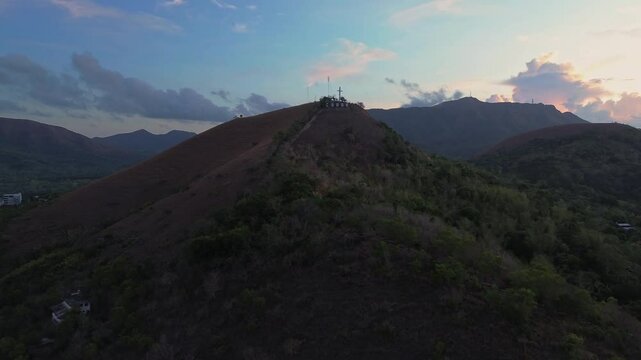 Aerial view approaching Mount Tapyas at dawn with the hilltop cross silhouetted above forested ridges in Coron Palawan
