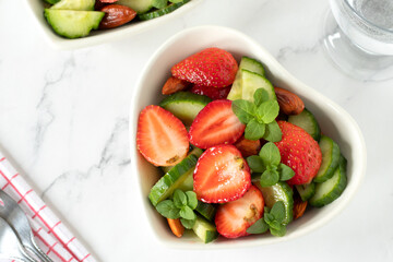 Strawberry cucumber salad with fresh mint and almonds in heart shaped bowls on white kitchen table. Top view. Healthy organic summer food.