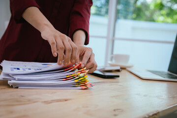 Close-up of businesswoman in office sorting through large amount of financial documents and files,...