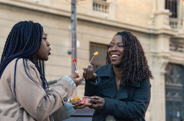 Two smiling friends sharing fruit outdoors in urban setting
