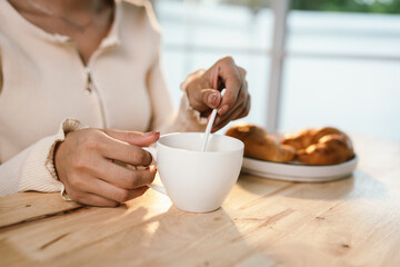 A woman enjoys a peaceful morning breakfast, holding a warm cup of coffee and a slice of bread in soft sunlight, embracing simplicity.