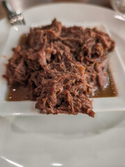 Braised beef overflowing small white square bowl on restaurant table