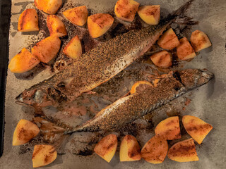 Two mackerel fish baking with potatoes and spices on baking sheet