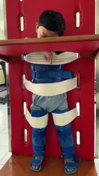 A child living with cerebral palsy is undergoing physiotherapy, to stimulate standing using a standing frame in the hospital, wearing AFO shoes, the child is seen asleep