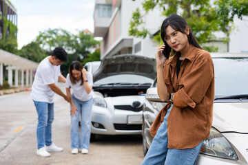 Fototapeta premium Asian Woman drivers call insurance after a car accident before taking pictures and sending insurance. Car Accident Emergency, while another person tends to a passenger with an injury.