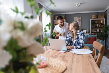 Young couple working remotely at home, analyzing documents and data, using laptop in cozy modern...