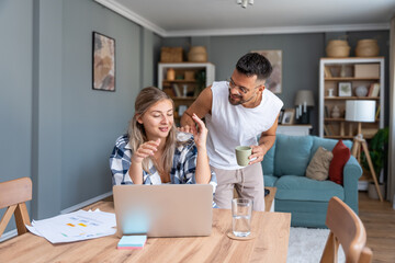 Obraz premium Young couple working remotely at home, analyzing documents and data, using laptop in cozy modern living room, discussing financial reports and business strategy. Couple goals, simple living support.
