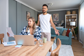 Young couple working remotely at home, analyzing documents and data, using laptop in cozy modern...