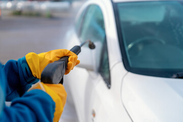 A person wields a high-pressure nozzle, blasting away dirt from a gleaming white car at a...