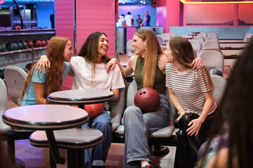 Four female friends are sitting, talking, and laughing at the bowling alley