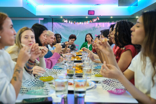 Multi ethnic group of students eating pizza together in their university cafeteria, having fun and socializing during lunch break