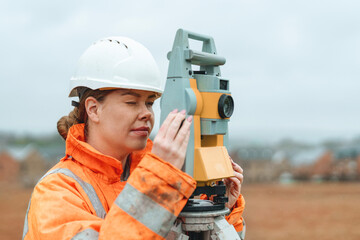 Female Construction surveyor using surveying equipment on building site while wearing bright...