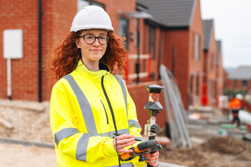 Portrait of confident female land surveyor with long hair in bright safety gear using surveying...