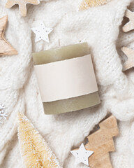 Green pillar candle with blank label on white sweater near wooden Christmas decor, mockup