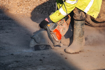 Construction worker  cutting asphalt road surface with petrol power concrete saw and diamond blade during roadworks