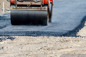 Heavy roller compacts fresh asphalt on a newly constructed road section during daytime work hours...