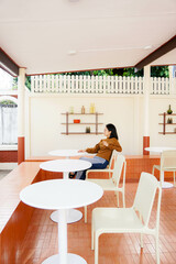 Joyful brunette curly woman in trendy pants and shirt smiles and looks out to view Pretty lady in jeans sits on chair in cafe