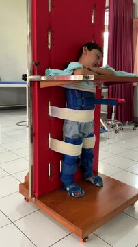 A child living with cerebral palsy is undergoing physiotherapy, for stimulation standing in the hospital, wearing AFO shoes, the child is seen asleep