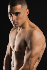 Fototapeta premium Confident shirtless man with muscular build posing against dark background. Lifestyle. Sport.