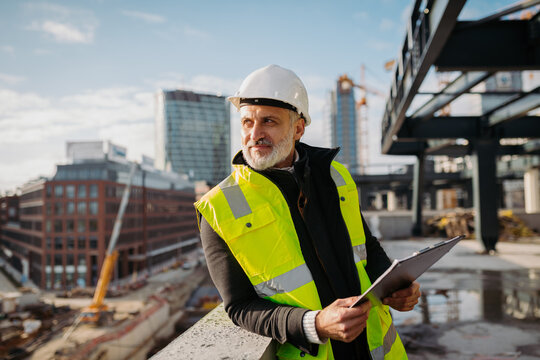 Engineer checking building documentation on clipboard at construction site.